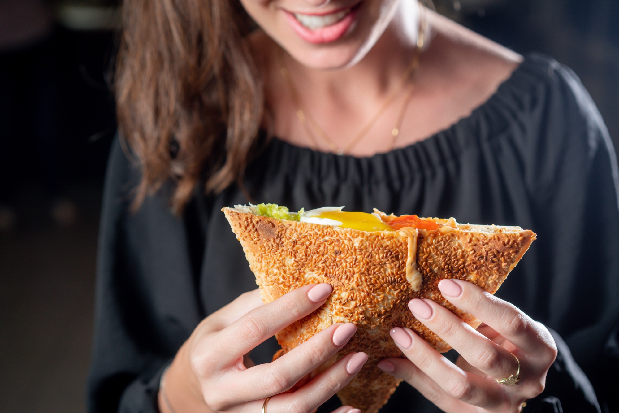 A customer smiling over a sesame toast filled with egg, salsa and cheese