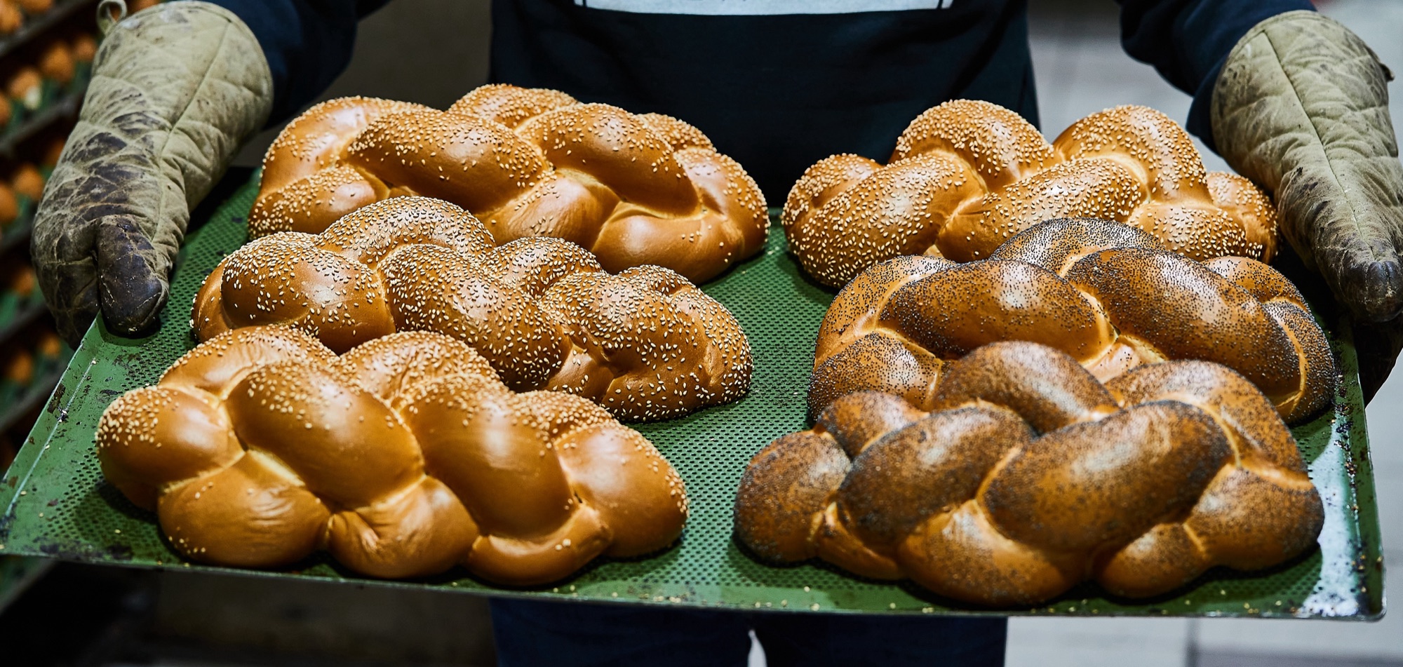 A baker carrying a tray of freshly braided sesame and poppy challah
