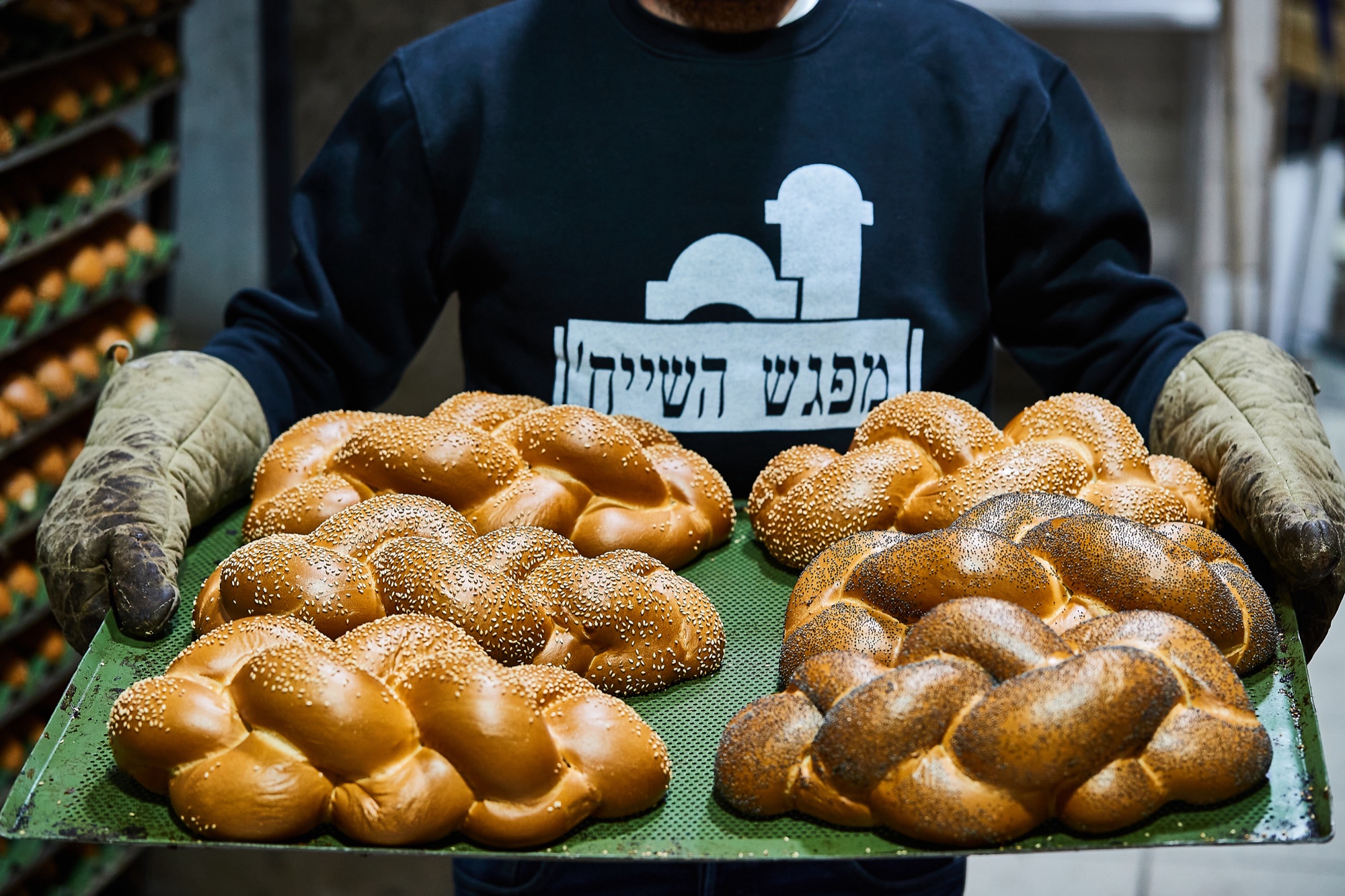 A TABUNA baker carrying a green tray of sesame and poppy-seed challah